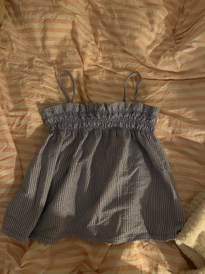 Randig blå linnetopp med smock - Säljer en randig blus som är  blå och vit, linnetopp med smock upptill och tunna axelband. Toppen är luftig och har en loose passform, perfekt för varma dagar. Materialet känns som bomull och ger en skön känsla mot huden. Skriv om ni har frågor💗💗