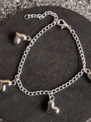 Silverfärgat armband med hjärtberlocker Rostfritt Stål  - Snyggt handgjort armband i silverfärgat rostfritt stål med flera små hjärtberlocker som hänger längs en tunn kedja. Armbandet har ett klassiskt karbinlås och justerbar längd. Perfekt accessoar för dig som gillar detaljer med romantisk vibe.