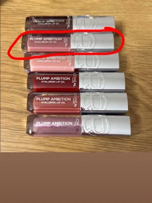 L'Oréal Plump Ambition läppglans - Säljer ett L'Oréal Paris Plump Ambition läppglans i en snygg röd nyans. Tuben har en silvrig kork med L'Oréal-logga och transparent plast som visar färgen. Perfekt för dig som vill ha fylliga och glansiga läppar med en hint av färg. Inte använd!