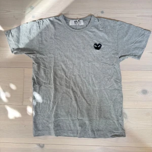Grå T-shirt från Comme des Garçons - Grå t-shirt från Comme des Garçons Play med dem klassiska hjärt-loggan. Bättre skick än vad det ser ut som på bilden, lite skrynklig pga förvaringen bara! OBS CDG är små i storlekarna!