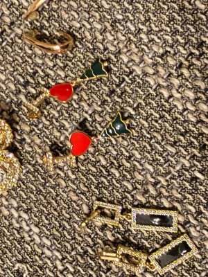 Hjärtformade örhängen med guld - Unika örhängen i guldton med röda hjärtan och gröna detaljer. Hängande modell med gnistrande stenar längs staven och triangelformad grön topp. Perfekta för dig som vill sticka ut med färg och lekfull design.