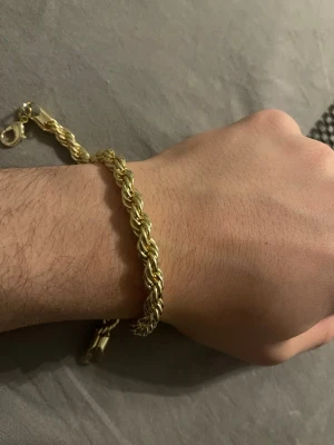 Guldtonat  armband cordell  - Snyggt armband i guldtonad metall med tvinnad design som ger en cool och modern look. Armbandet har en klassisk karbinhake som lås och passar perfekt för dig som gillar stilrena accessoarer med lite extra edge.