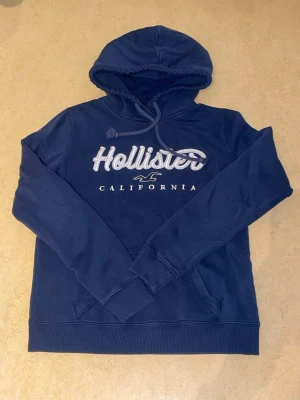 Mörkblå Hollister hoodie  - Mörkblå hoodie från Hollister 💙 Har använts ett par gånger men inte sönder eller sliten nånstans. Den är liten i storleken så rekommenderar den för dig som har XS eller S. Priset har en liten chans att sänkas men helst inte med tanke på att den är nästan helt ny 🫶🏼