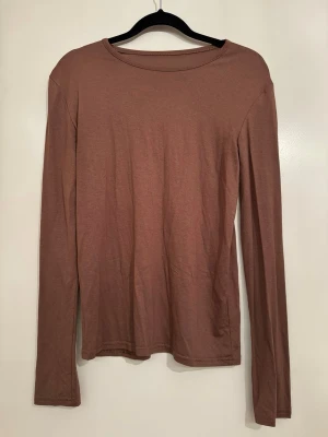 Brun långärmad basic topp - En enkel och stilren brun långärmad topp i mjukt och stretchigt material. Modellen har rund halsringning och raka ärmar, perfekt att matcha med jeans eller kjol för en clean look. Köpt utomlands. Storlek står inte med men skulle säga att den är i storlek XS/S. Bröstmått är ca 72cm. 