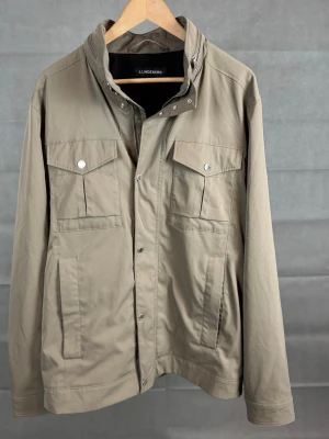 J lindeberg fieldjacket bailey - J.Lindeberg fieldjacket, mycket eftertraktad modell| Färg: Beige | Storlek: XL, kan även passa L | Skick: Otroligt bra skick, inga defekter | Hör av dig vid frågor och funderingar! 