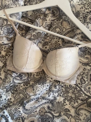 Beige push-up bh med spetsdetaljer - Säljer en beige push-up bh med tunna axelband och fina spetsdetaljer på kuporna. Bh:n har bygel och vadderade kupor för extra stöd och form. Perfekt för dig som vill ha en enkel men ändå elegant bh. B-kupa 