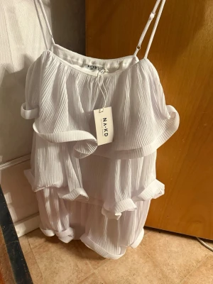 Vit volangklänning från NA-KD - Supersöt vit kortklänning från NA-KD med tunna axelband och flera lager volanger. 