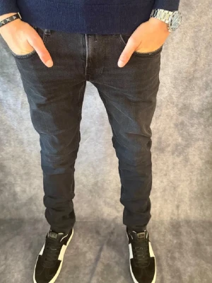 Svarta replay anbass  - Säljer ett par svarta replay anbass med klassisk femficksdesign och normal midja. Jeansen har en snygg tvättad look och smal passform som sitter tajt längs benen. Perfekta för dig som gillar en modern och stilren stil. Obs litet håll mellan benen men lätt att fixa!