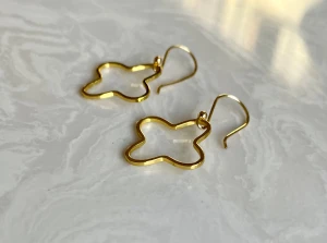 Guldiga örhängen i blomform, stainless Steel  - Snygga örhängen i guldton med öppen blomformad design. De har en enkel krok och är tillverkade i stainless Steel med blank finish. Perfekta för dig som vill ha en lekfull och trendig accessoar som sticker ut.