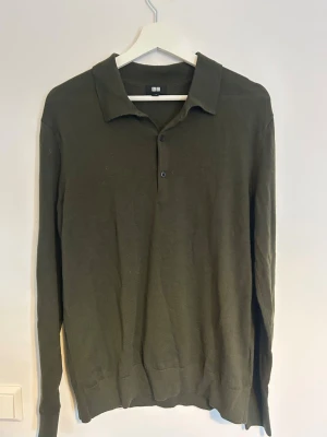 Olivgrön pikétröja från Uniqlo - Snygg olivgrön långärmad pikétröja från Uniqlo med klassisk krage och tre knappar framtill. Tillverkad i 100% merinoull som passar perfekt för lager på lager. Enkel och stilren design som funkar till det mesta.