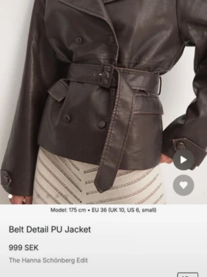 Brun skinnjacka med bälte NA-KD - Snygg mörkbrun skinnjacka från NA-KD med bälte i midjan och dubbelknäppning. Jackan har bred krage, dekorativa knappar och fickor framtill. Perfekt för dig som vill ha en trendig och stilren look.
