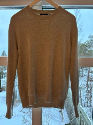 Beige stickad tröja med rund hals - En stilren beige stickad tröja med rund halsringning och ribbade muddar vid ärmslut och nederkant. Tröjan har en enkel, klassisk design och är perfekt för lager-på-lager. Passar dig som gillar en clean och avslappnad look.