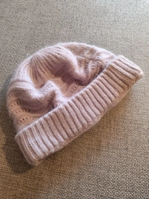 Ljuslila stickad mössa - Mysig ljuslila stickad mössa med bred vikt kant och diskret hålmönster. Tillverkad i mjukt garn som känns skönt mot huden och ger en avslappnad look. Perfekt för kalla dagar när du vill hålla dig varm och ändå se snygg ut.