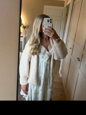 Vit kortklänning med blommor och knyt - Söt vit kortklänning med små gula citroner, puffärmar och knyt i ringningen. Klänningen har volangdetaljer och en luftig passform, perfekt för varma dagar. Tillverkad i ett lätt bomullstyg. Använts lite och inga defekter alls!❣️