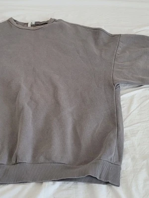 Grå oversized sweatshirt - En enkel och stilren grå sweatshirt i oversized modell. Tröjan har rund halsringning, ribbade muddar vid ärmslut och nederkant samt en avslappnad passform. Perfekt för en chill och casual look. Materialet känns mjukt och bekvämt, troligtvis bomull eller bomullsblandning.