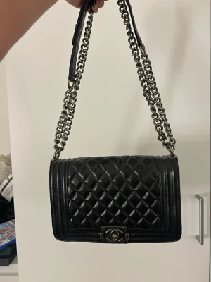 Svart Chanel väska - Fake! Svart Chanel väska. Bandet går att ha kort och långt. Mörksilvriga detaljer. Ungefär 17*24cm så mellanstor 