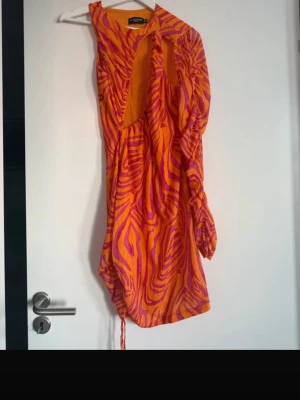 Orange och rosa klänning  - Säljer en färgstark kort omlottklänning från NA-KD i orange och rosa med zebramönster. . Perfekt för dig som vill sticka ut med en unik look. Strl 42 