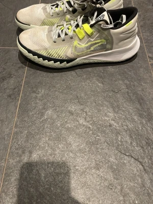 Nike Kyrie vita och neongula sneakers - Säljer ett par Nike Kyrie basketskor i vitt med neongula och svarta detaljer. Skorna har meshmaterial för bra ventilation, mönstrad sula för grepp och coola snören i grått och vitt. Perfekta för basket eller streetstyle.