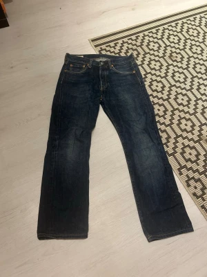 Mörkblå Levi's Premium jeans - Säljer ett par mörkblå jeans från Levi's Premium med klassisk rak passform och fem fickor. Jeansen har snygga slitningar och kontrastsömmar. Perfekta för dig som gillar en tidlös och stilren look. Uppsydda i affär, så ytterbenslängden är ca 94 cm.