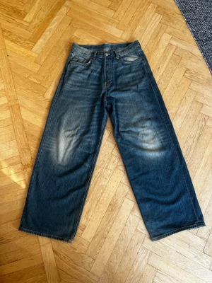 Blåa baggy jeans med vintage-look - Säljer ett par blåa jeans med breda ben och klassisk femficksdesign. Jeansen har en snygg tvättad finish med ljusare partier på låren och raka ben. Perfekta för en avslappnad och trendig stil. Materialet är kraftig denim i bomull. Modellen ser ni på sista bilden.