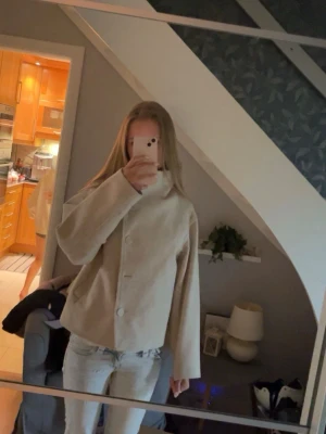 Beige manchesterjacka med knappar - Stilren beige jacka i manchester med stora knappar framtill och rak passform. Jackan har lång ärm och en enkel, minimalistisk look som passar till det mesta. Perfekt för dig som gillar en clean och modern stil.