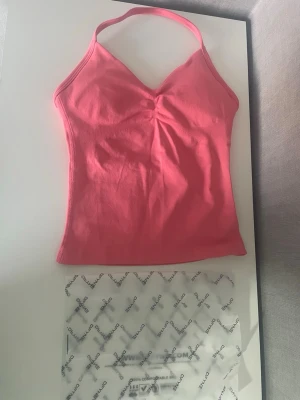 DFYNE träningstopp i rosa - Säljer en snygg rosa linnetopp från DFYNE med smala axelband och v-ringad hals. Toppen är figurnära och har en enkel, stilren design utan mönster. Perfekt för dig som gillar en sportig och trendig look.