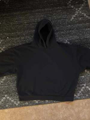 Mörkgrå croppad hoodie - En stilren svart halvt croppad hoodie med luva och långa ärmar. Hoodien har en enkel design utan tryck eller detaljer och är gjord i mjukt sweatshirtmaterial. Perfekt för en avslappnad och trendig look.