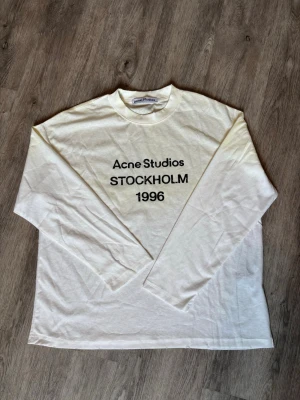 Acne studios long sleeve - Vit långärmad topp från Acne Studios med tryck 'STOCKHOLM 1996' framtill. Klassisk rak passform och rund halsringning. Perfekt för dig som gillar minimalistisk stil och vill ha en enkel men snygg statement-top. Tillverkad i mjuk bomull.