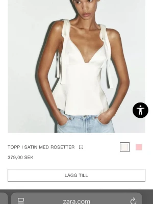 Vit satinlinnetopp med rosetter - Snygg vit linnetopp i satin med breda axelband som knyts i rosetter. Toppen har v-ringning och figurnära passform, perfekt till jeans eller kjol. Materialet ger en lyxig känsla och den är ärmlös för en fräsch look.