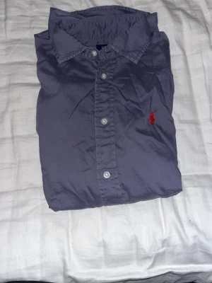 Polo Ralph Lauren Oxfordskjorta Grå M – Relaxed Fit - Säljer en äkta Polo Ralph Lauren-skjorta i grå färg, storlek M (Relaxed Fit). Klassisk modell med röd broderad Polo-logga på bröstet. Mycket bra skick utan hål eller fläckar. Passar perfekt till både vardag och mer uppklädda tillfällen. Pris kan diskuteras vid snabb affär.