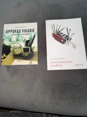 Två kursböcker om skolan - Säljer två kursböcker: 'Uppdrag vikarie – Ledarskap i klassrummet' och 'Lärarassistentens handbok'. Perfekta för dig som pluggar till lärare eller lärarassistent. Ena boken har ett färgstarkt omslag med klocka och pennor, den andra är vit med en bild på en schweizisk armékniv.