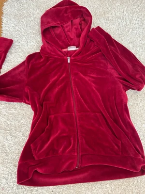 Röd velourhoodie från Isolde - Mysig röd hoodie i mjuk velour från Isolde. Dragkedja framtill, två stora fickor och en rejäl huva. Perfekt för chill dagar och när du vill ha något riktigt bekvämt. Klassisk passform och snygg färg som sticker ut.