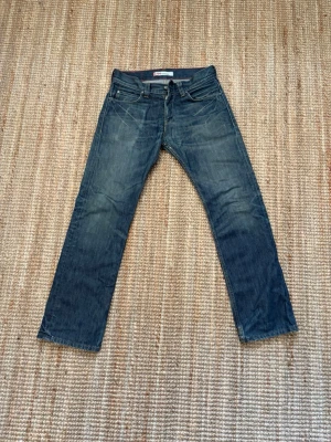 Distressed Slim Jeans - Levis 507 Selvedge - Säljer ett par klassiska blå jeans med raka ben och lätt slitna detaljer. Jeansen har fem fickor, normal midja och kontrastsömmar. Perfekta för en avslappnad och stilren look. Materialet är denim i bomull.