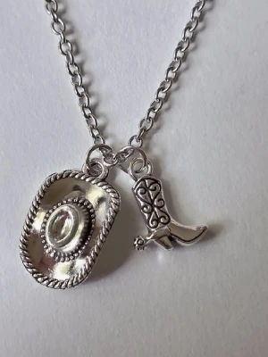 Halsband med cowboyhatt och cowboyboots 🤠 - Silvrigt halsband med två hängen: en detaljerad cowboyhatt och en westerninspirerad stövel. Kedjan är av metall och har en klassisk länkdesign. Perfekt accessoar för dig som gillar westernstil yeeehaaa 🤠 materialet rostfritt stål 