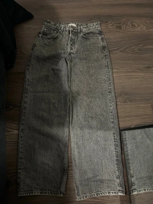 Grå raka jeans från Ginatricot  - Säljer ett par grå raka jeans från Ginatricot med låg midja och fem klassiska fickor. Jeansen har en tvättad look och breda ben.