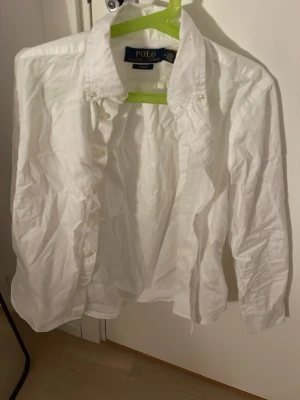 Vit skjorta från Polo Ralph Lauren - Klassisk vit skjorta från Polo Ralph Lauren i slim fit-modell. Skjortan har långa ärmar, knappar framtill och en stilren krage. Tillverkad i bomull, perfekt för en clean och tidlös look.