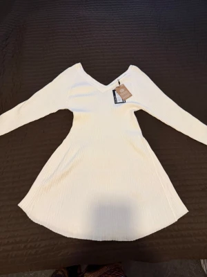 Vit ribbad långärmad klänning - Snygg vit ribbad klänning med lång ärm och v-ringning. Klänningen har en kort längd och är tillverkad i ett mjukt material. Perfekt för dig som gillar en enkel men stilren look. Helt ny med prislapp.