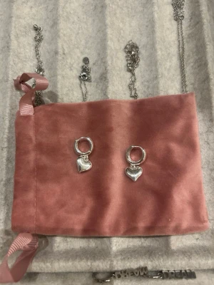 Silverörhängen med hjärtberlocker - Säljer ett par stilrena örhängen i silverfärg med små hjärtformade berlocker. Örhängena har en klassisk ringform och hjärtana hänger snyggt nedanför. Perfekta för dig som gillar enkla men söta accessoarer.
