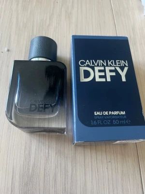 Calvin Klein Defy Eau de Parfum 50 ml - Calvin Klein Defy Eau de Parfum i 50 ml flaska. Flaskan är mörkblå med stilren design och svart kork. Förpackningen är också mörkblå med guldtext. En modern och maskulin doft som passar dig som vill sticka ut. Produkten är oandvänd.
