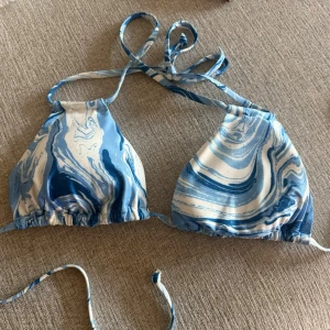 Blåvit bikiniöverdel med marmorprint strl 44 - Snygg trekantsbikini med blått och vitt marmormönster. Klassisk modell med knyt i nacke och rygg, perfekt för sommardagar på stranden. Materialet känns mjukt och följsamt mot huden.