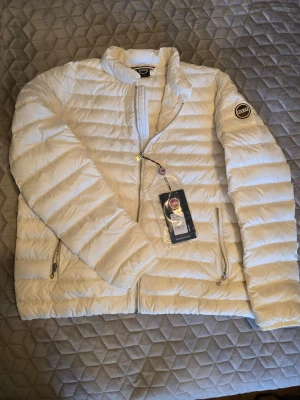 Vit dunjacka från Colmar - Snygg vit dunjacka från Colmar med quiltad design och två dragkedjeförsedda fickor. Jackan har logotyp på ärmen. Perfekt för svala dagar och har en stilren look som passar till många outfits.