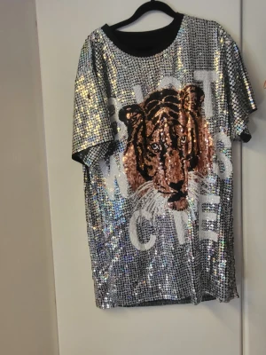Glittrig t-shirt med tigertryck - Säljer en riktigt cool t-shirt med glittriga paljetter över hela och ett stort tigertryck på framsidan. T-shirten har korta ärmar och en svart rund halsringning. Perfekt för dig som vill sticka ut och gillar djurmotiv.
