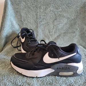 Nike Air svartvita sneakers - Svarta Nike Air sneakers med vit sula och vit swoosh på sidan. Skorna har mesh och syntetmaterial på ovansidan, klassisk snörning och en synlig Air-dämpning i hälen. Perfekt för dig som gillar sportig stil och komfort.