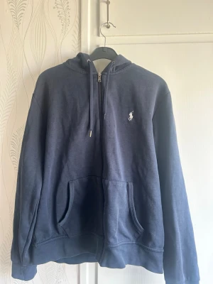  Polo Ralph Lauren hoodie - Mörkblå hoodie med dragkedja från Polo Ralph Lauren. Klassisk design med huva och snören. Det är en storlek M