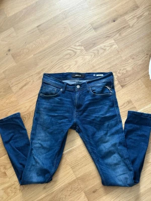 Blå slim fit jeans från Replay - Snygga blå slim fit jeans från Replay med klassisk femficksdesign och diskret slitning på framsidan. Jeansen har en bekväm passform och är tillverkade i stretchigt denim-material. Perfekt för dig som vill ha en modern och stilren look.