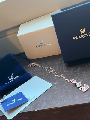 Swarovski halsband med rosa kristaller - ORIGINALPRIS nästan 2,000 krSupersnyggt halsband från Swarovski i roséguld med en ikonisk svanberlock dekorerad med gnistrande rosa och klara kristaller. Kedjan är tunn och elegant, och halsbandet kommer med originalask och certifikat. Perfekt accessoar för att lyfta din stil.
