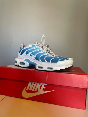Nike Air Max Plus blå och vita sneakers - Nike Air Max Plus sneakers i blått och vitt med ikoniska vågmönster och synliga Air-bubblor i sulan. Skorna har TN-logga på hälen och är tillverkade i mesh och syntetmaterial. Skorna har en liten defekt på framsidan men annars är de i bra skick! Tveka inte att höra av er🌟 nypris runt 3500kr
