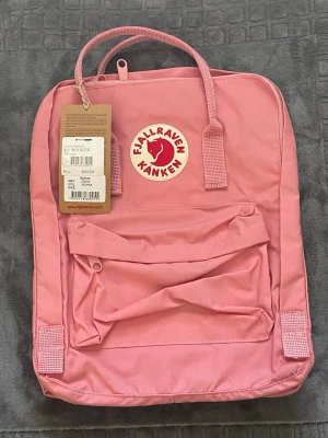 Kånken  - Fjällräven Kånken ryggsäck i rosa. Ryggsäcken har ett huvudfack med dragkedja, en framficka med dragkedja och två öppna sidofickor. Den har dubbla handtag upptill och justerbara axelremmar. Inuti finns en sittdyna.
