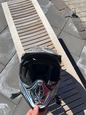 AGV motocrosshjälm med blå detaljer - Motocrosshjälm från AGV med coolt mönster i svart, silver och blått. Hjälmen har ett robust visir och ventilerad front, samt vadderad insida för extra komfort. Perfekt för dig som vill ha en snygg och säker hjälm till äventyr på två hjul.