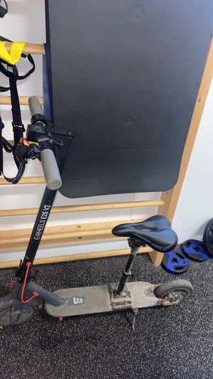 Svart elscooter E-Wheels E2S V2 med sadel - Säljer en svart elscooter E-Wheels E2S V2 med sadel och digital display som visar hastighet och batterinivå. Scootern har grå handtag, robust ram och fotplatta med mönster. Perfekt för smidig transport i stan.